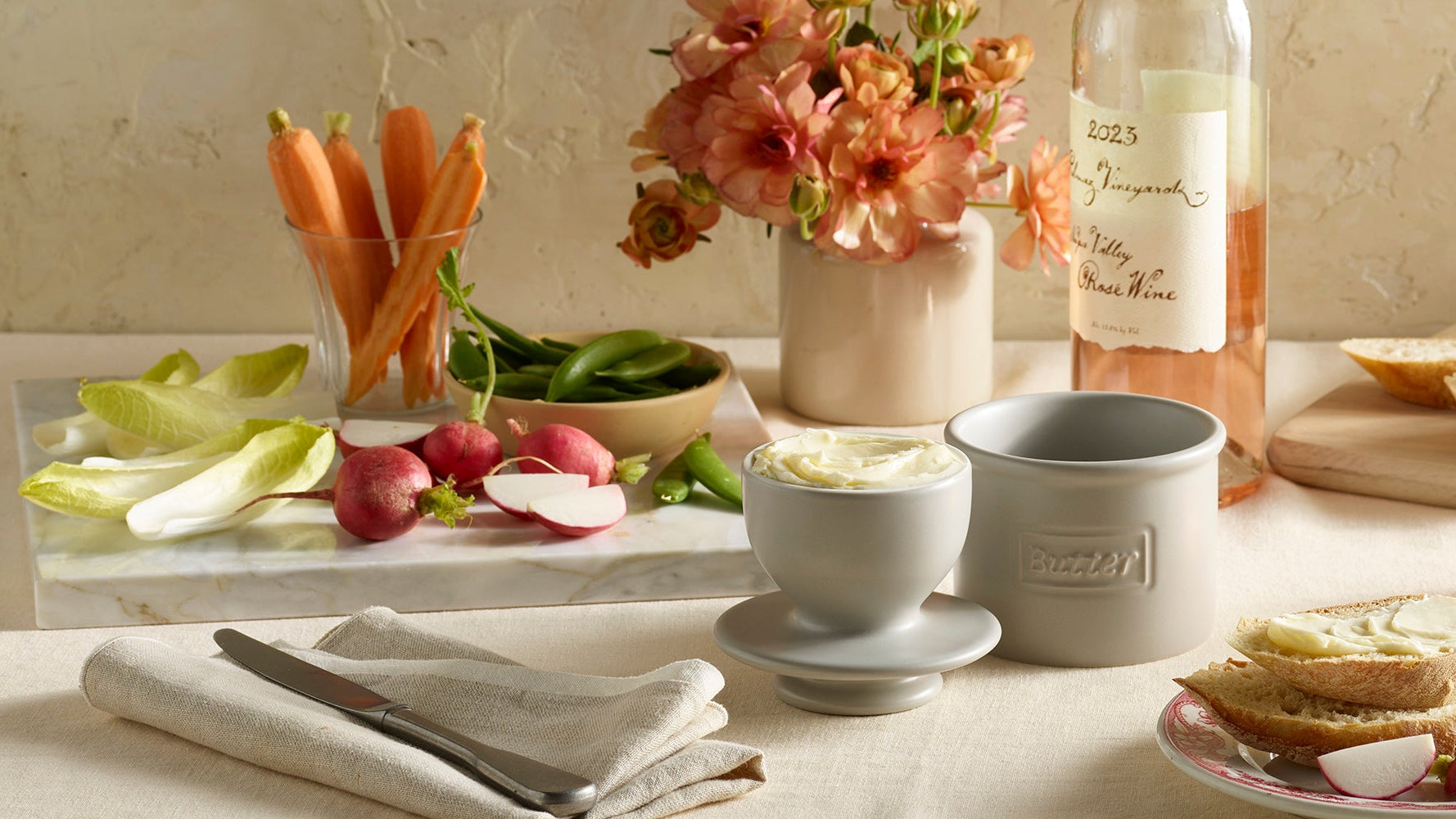 Table setting with bread, wine, and appetizers on a light background butter bell crock